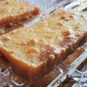 This photo shows the completed recipe for Tofu Jerky with Peanut Sauce - Dehydrator Method by Reese Amorosi for GlamorosiCooks.com. There is a rectangular piece of tofu that has been marinated in peanut sauce and then dried in a dehydrator - it is still in the appliance and the slotted drying trays are visible.