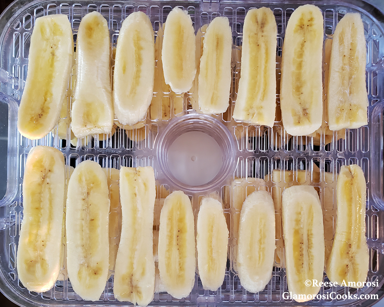 This photo shows raw fruit for Banana Jerky - Dehydrator Method by Reese Amorosi for GlamorosiCooks.com. The banana slices are on a slotted tray inside of an electric dehydrator.