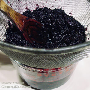 Blackberry Syrup Recipe by Reese Amorosi for GlamorosiCooks.com. In this photos the berries are in a pot and are being broken down with a potato masher. 