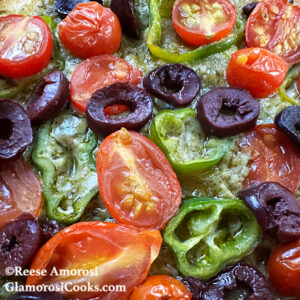 This photo shows the completed recipe for Easy Flatbread Pizza by Reese Amorosi for GlamorosiCooks.com. The flatbread is topped with pesto, cheese, tomatoes, Shishito peppers and olives.